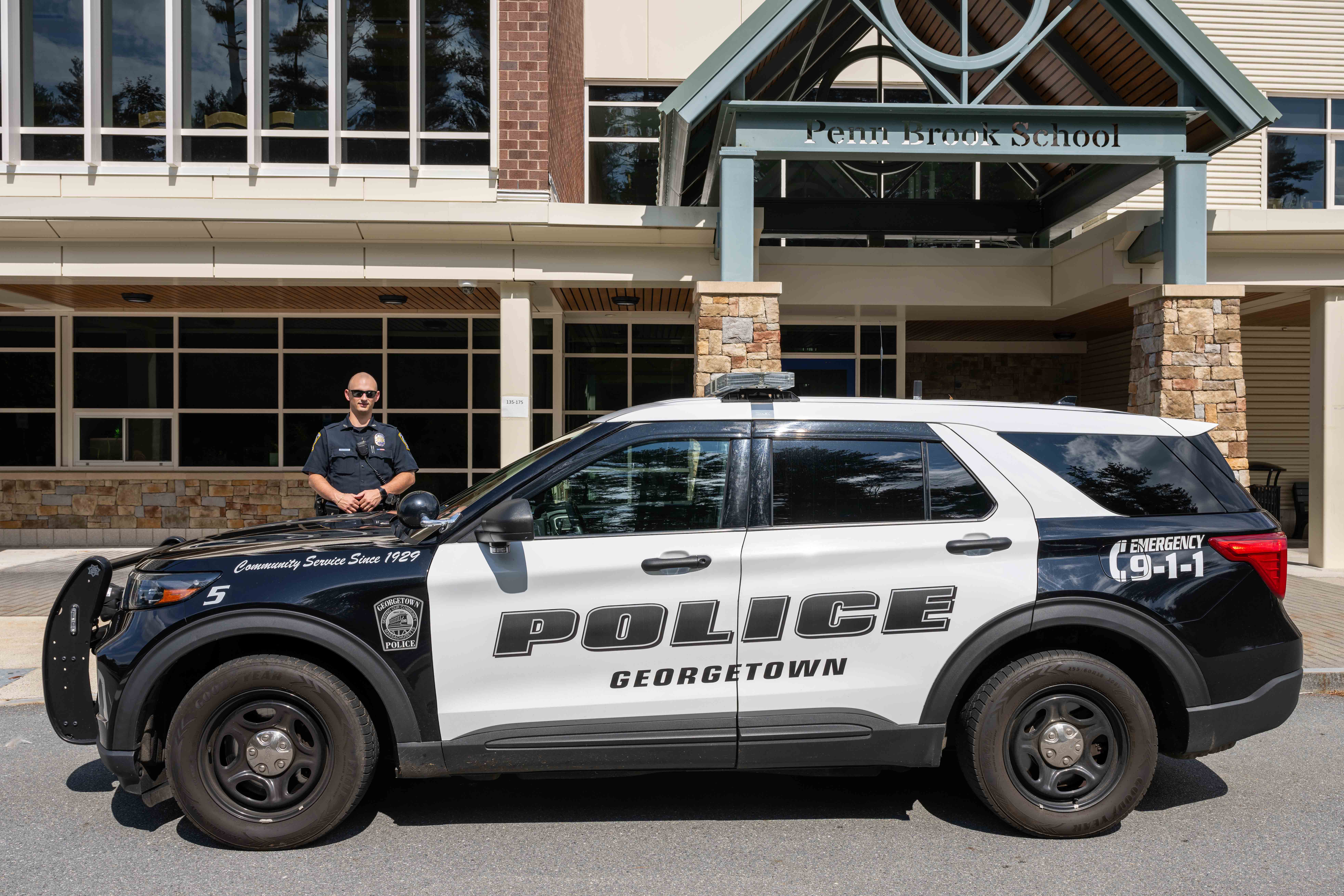 Police officer stands behind a parked cruiser.